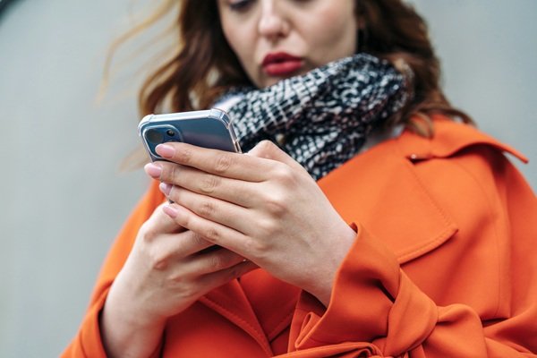 Woman in orange coat using smartphone outdoors