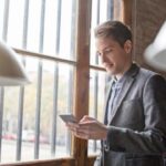 Mann im Büro nutzt Smartphone am Fenster.