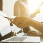 Person zeigt mit Stift auf Laptop-Bildschirm im Büro.