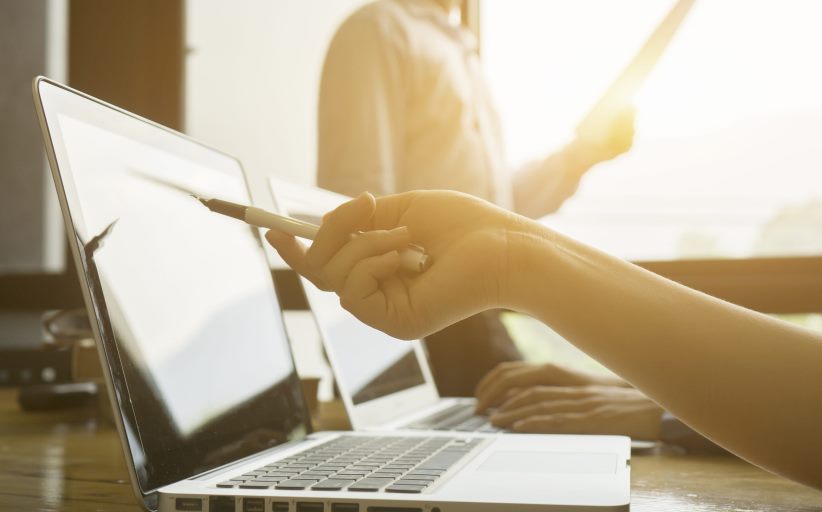 Person zeigt mit Stift auf Laptop-Bildschirm im Büro.