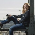 Frau mit Kaffeebecher sitzt auf Brücke in München.