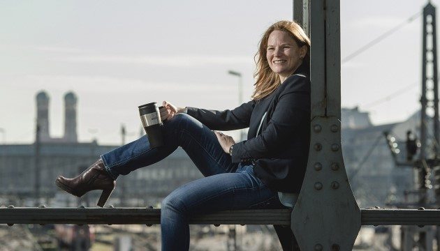 Frau mit Kaffeebecher sitzt auf Brücke in München.