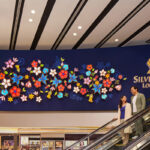 Paar auf Rolltreppe unter Blumenwand im SilverKris Lounge.