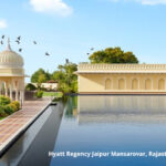 Edificación alargada, de una planta, se refleja en espejo de agua en el hotel Hyatt Regency Jaipur Mansarovar, en Rajasthan, India. También, se ve cúpula de arquitectura islámica.