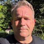 Person in garden under sunlight, surrounded by greenery.