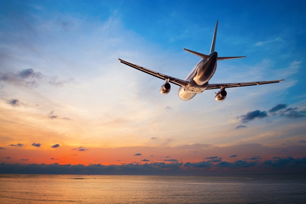 Airplane flying over ocean at sunset