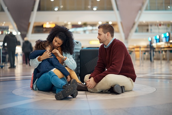 Family sitting on airport floor with suitcase
