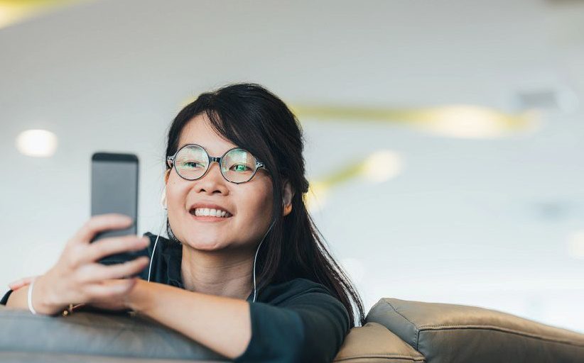 Mujer con lentes observando el celular y sinriendo.