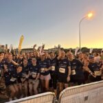 Participantes en carrera nocturna saludan y sonríen.