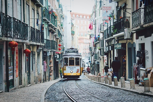 Un tranvía avanza por el medio de una calle colonial en una ciudad portuguesa. A cada lado, se ven casas de dos plantas y, en el fondo, un edificio.