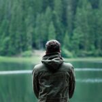 Hombre dando la espalda a la cámara, con chaqueta, mirando hacia un lago.