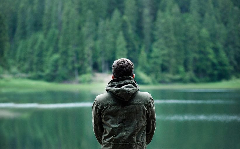 Hombre dando la espalda a la cámara, con chaqueta, mirando hacia un lago.