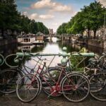 Varias bicicletas antiguas aparecen recostadas contra la baranda de un puente en un río de una ciudad europea.