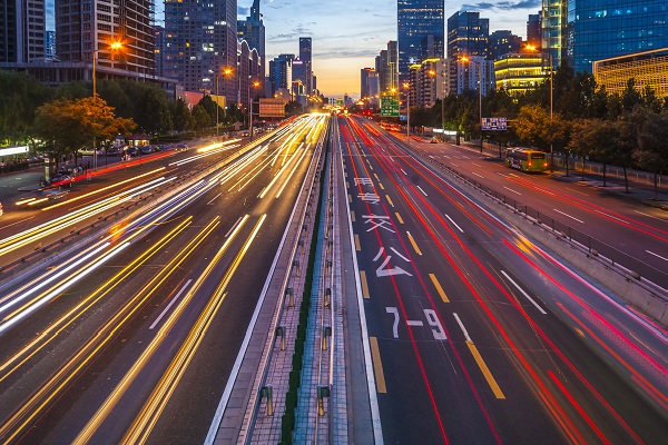 En una autopista de varios carriles, en una ciudad asiática, se ven haces de luces rojas, amarillas y blancas que indican el paso de autos a alta velocidad.