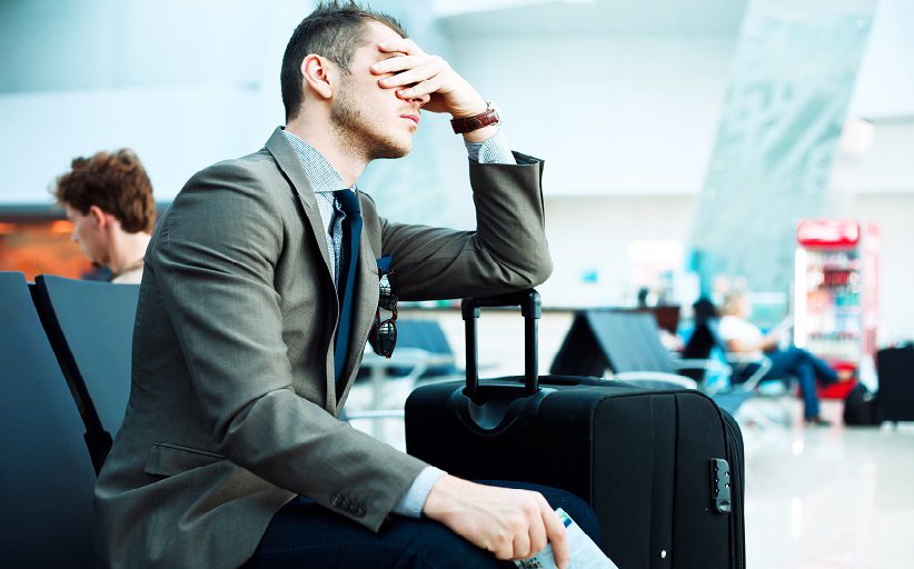 Hombre joven de negocios, sentado en la sala de espera de un aeropuerto, se lleva una mano al rostro en un gesto de preocupación