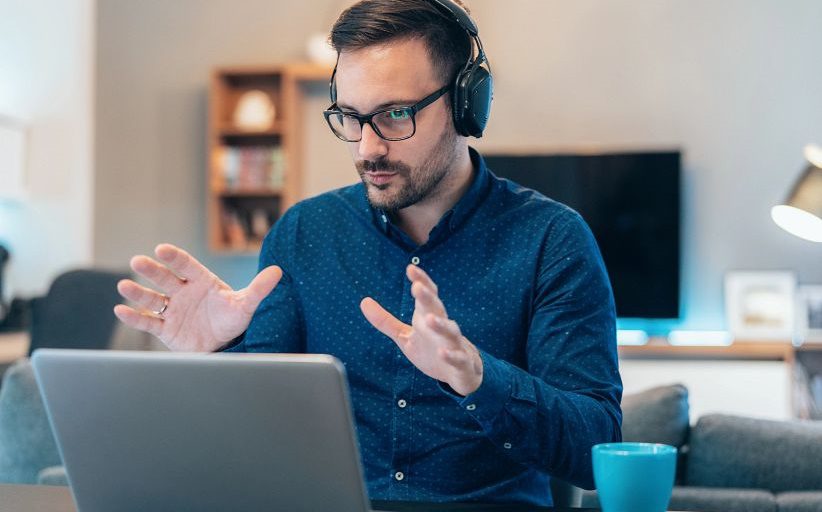 Hombre con gafas y audífonos explica algo mirando a la pantalla de una laptop.