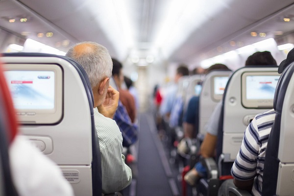 Foto del corredor de un avión en el que se ve, desde atrás, a varios pasajeros sentados y los respaldos de las sillas con las pantallas activas.