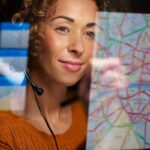 Mujer observa el mapa de una ciudad en el que se resaltan varias rutas, en colores verde, amarillo y rojo, en el reflejo de una pantalla.