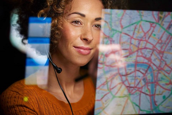 Mujer observa el mapa de una ciudad en el que se resaltan varias rutas, en colores verde, amarillo y rojo, en el reflejo de una pantalla.