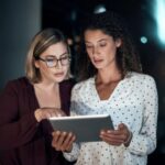 Dos mujeres de negocios analizando información en una tableta digital.