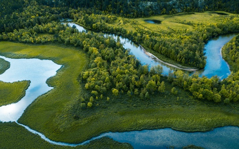 Vista aérea de un rio en medio del bosque y la pradera. Vuelos sostenibles.