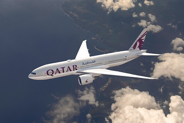 Imagen en contrapicado de un avión blanco, con el logo de Qatar Airways en la cola, que surca los aíres. Abajo, al fondo se ve el mar llegando a una costa montañosa.