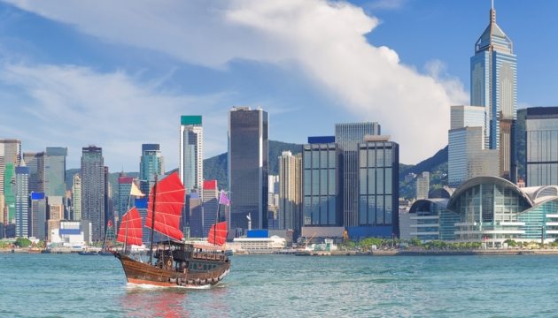 Un barco de velas rojas navega frene a una de las ciudades de China.