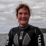 Claire Stephens, vice president, Global Client Team de BCD, sonríe en su traje de neopreno para nadar. Al fondo: el mar y un tramo de tierra firme.