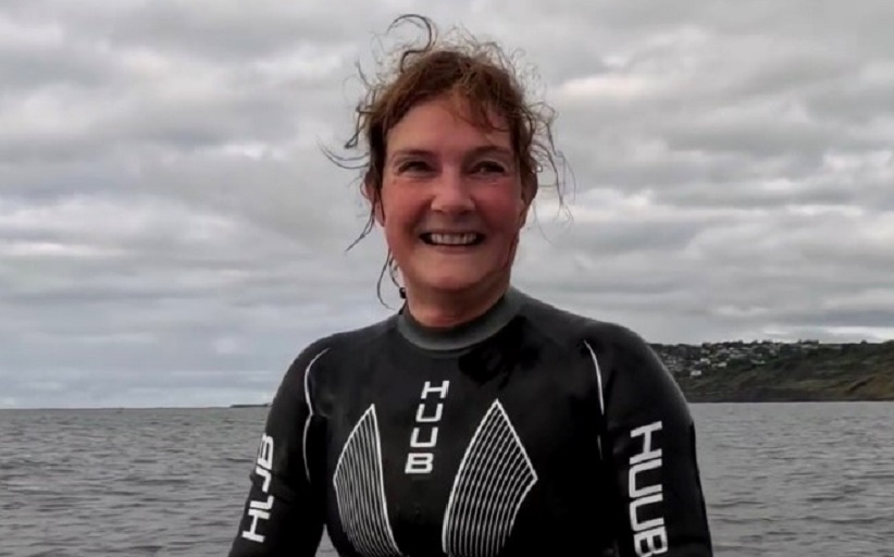 Claire Stephens, vice president, Global Client Team de BCD, sonríe en su traje de neopreno para nadar. Al fondo: el mar y un tramo de tierra firme.