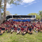 Más de un centenar de empleados de BCD están sentados sobre el césped, con un bus blanco en el fondo, en actividades de la iniciativa Making a Difference.