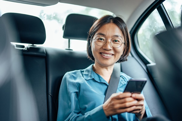 Smiling person using smartphone in car backseat.