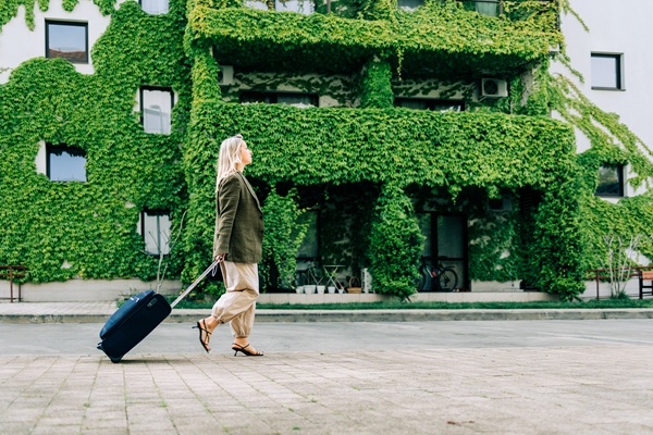 Woman walking with suitcase near ivy-covered building.