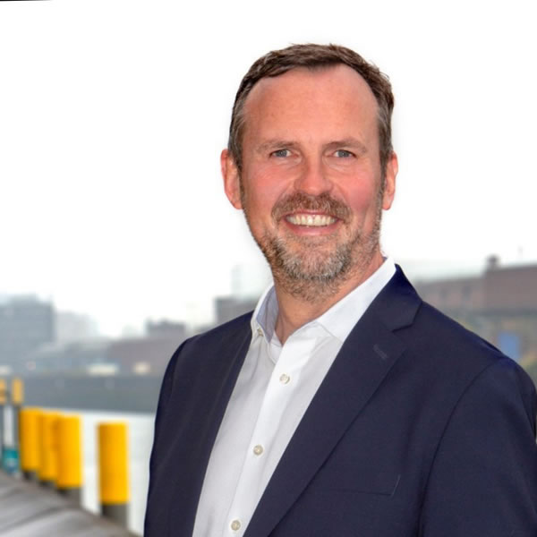 Lutz-Nauert-1 Homme souriant en costume près d'un quai.