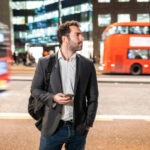 Man with smartphone stands near busy city street