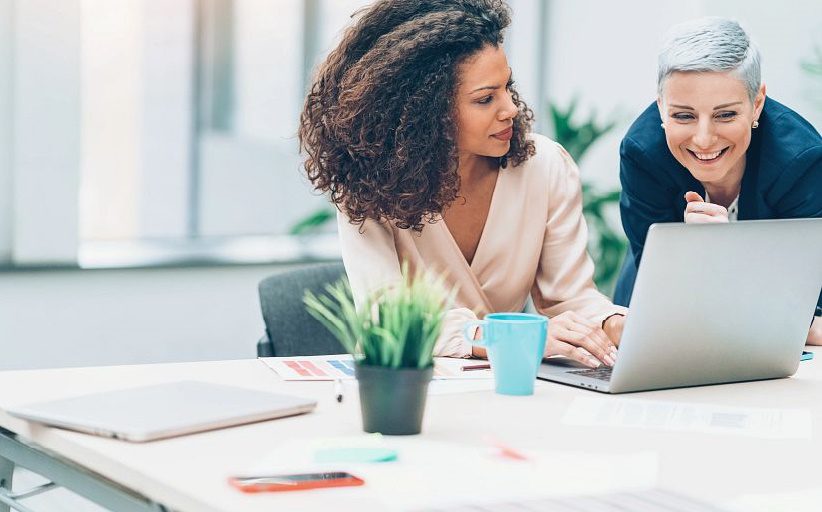 Des femmes professionnelles dans un bureau regardent ensemble l'écran d'un ordinateur portable.