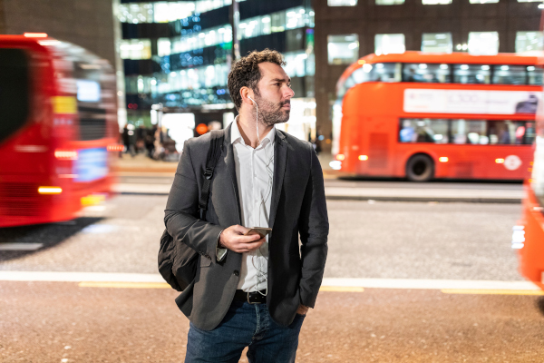 Man with smartphone stands near busy city street