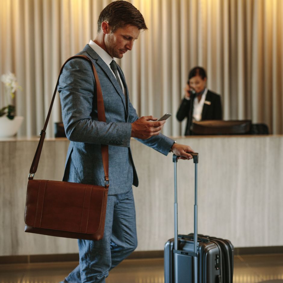 Business traveler checks phone beside suitcase at hotel reception
