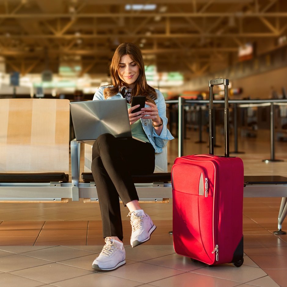 Traveler uses phone beside red suitcase at airport