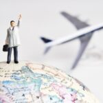 Miniatuurman op wereldbol met vliegtuig op achtergrond.