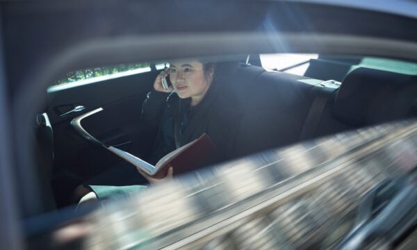 Vrouw in auto met telefoon en boek
