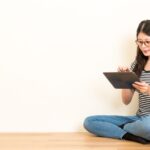 Vrouw leest zittend op de vloer met tablet.