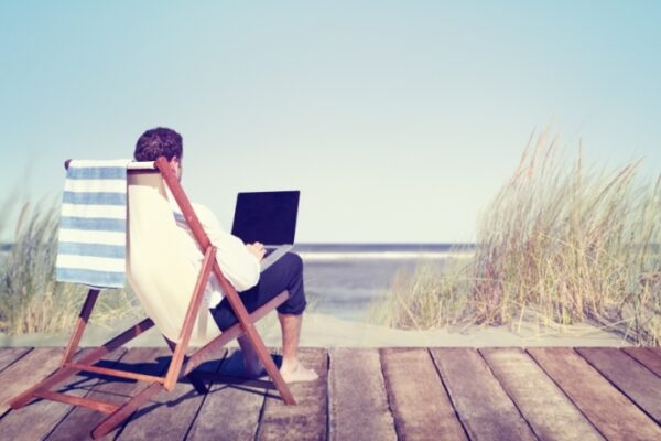 Persoon werkt op laptop, zittend bij de zee.