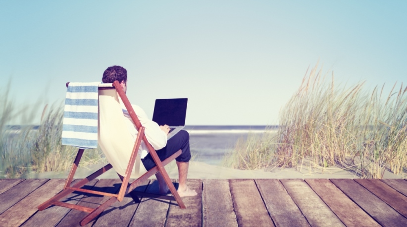 Persoon werkt op laptop, zittend bij de zee.