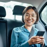 Smiling person using smartphone in car backseat.