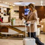 Woman with suitcase in hotel lobby using phone.