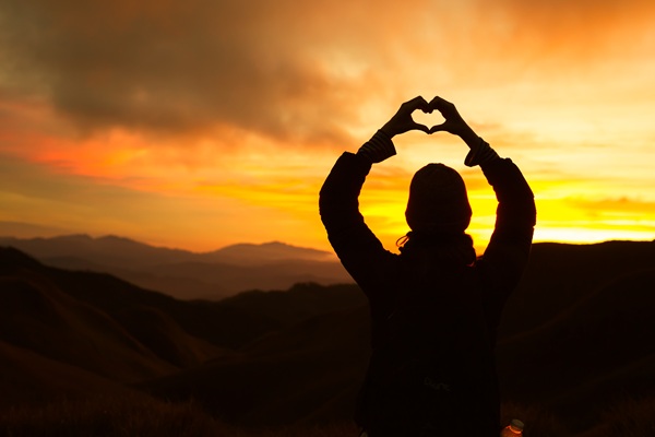 Silhouette forming heart shape at sunset over mountains