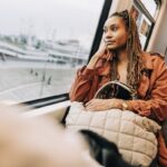 Woman gazing out train window, holding beige bag.