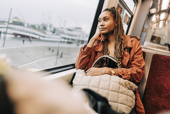 Woman gazing out train window, holding beige bag.