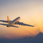 Airplane flying into sunset sky