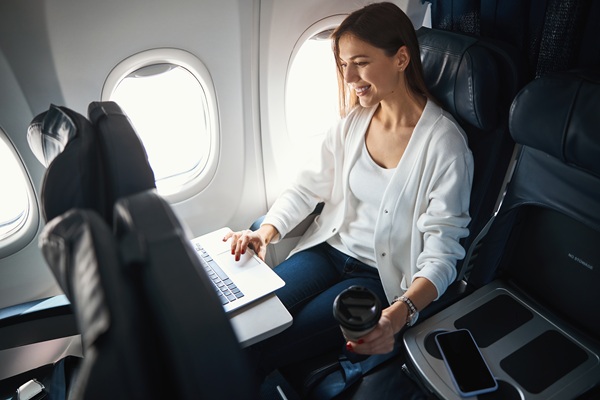 Woman using laptop on airplane with coffee